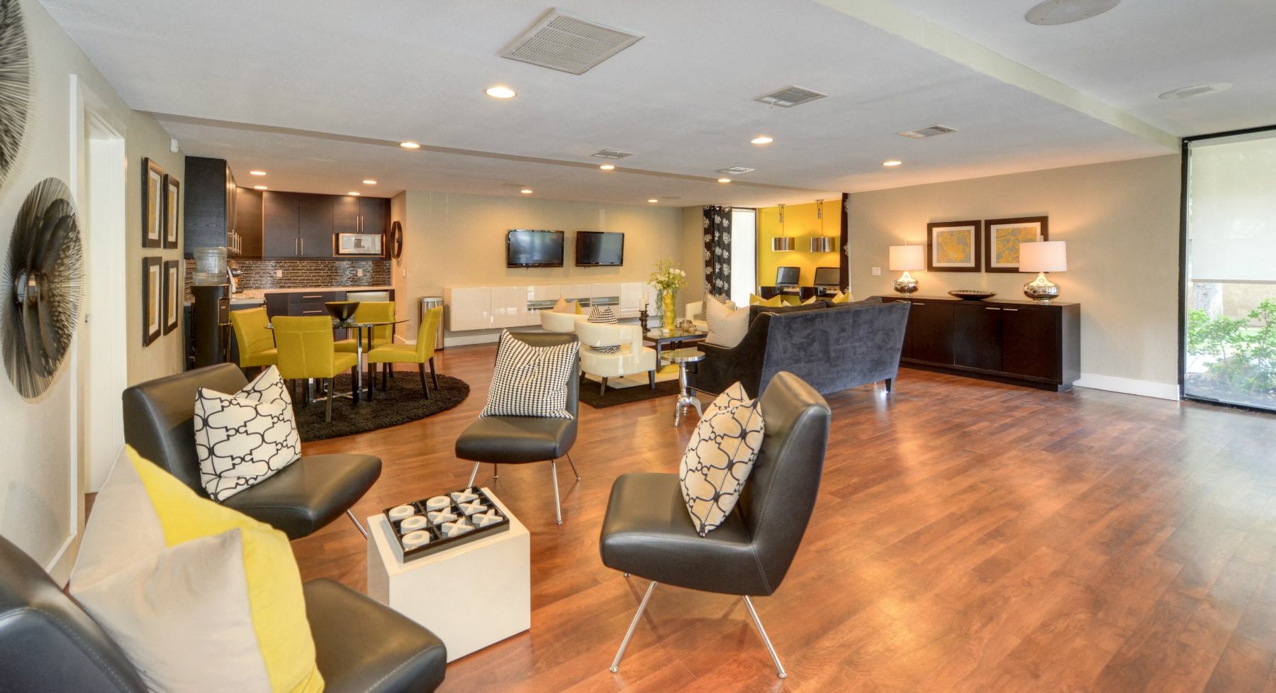 Clubhouse Lounge Area with Hardwood Inspired Floors, Black Sofa Chairs, Windows, and View of Kitchen Area